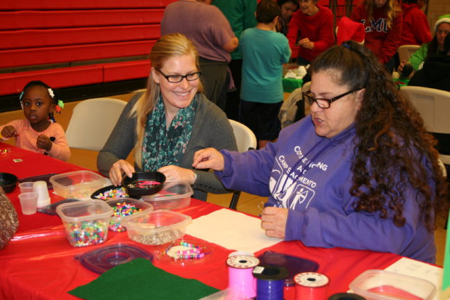 A volunteer helps a woman and child make jewelry