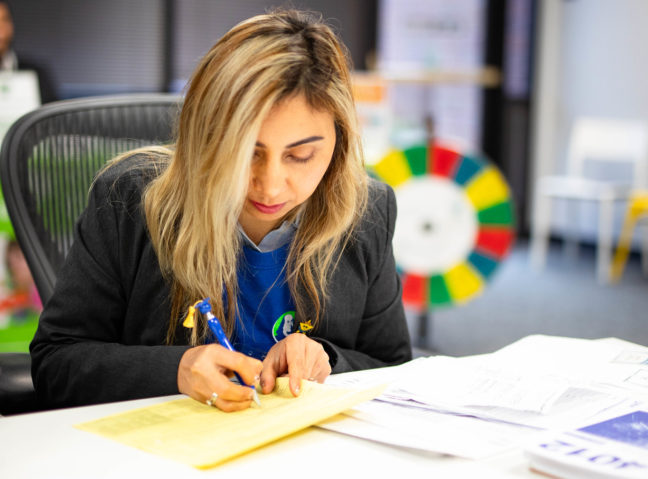A woman who is a Free Tax Prep volunteer looks at forms on a table and takes notes