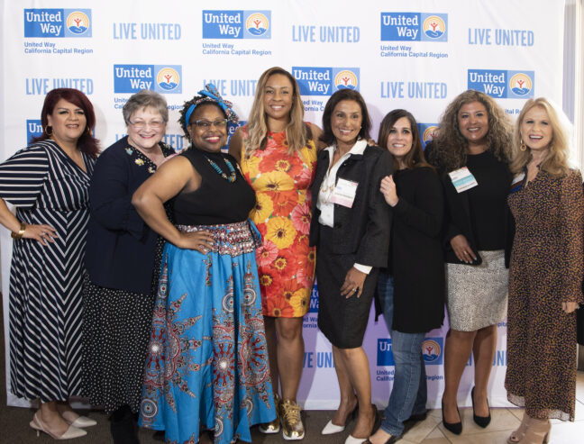 Eight women stand in front of a United Way background at a Women United event