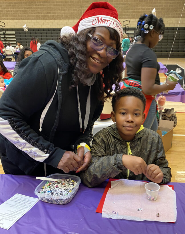 A Women’s Empowerment graduate in a Santa hat makes beaded bracelets as holiday gifts with her grandson at the annual Holiday Craft Party