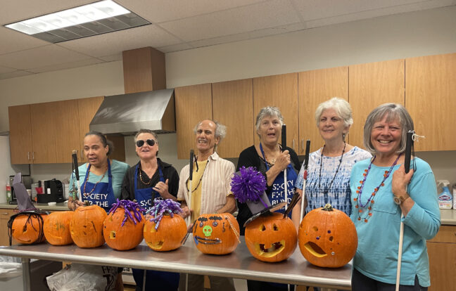 Six seniors at Society for the Blind stand with pumpkins they learned how to carve without sight