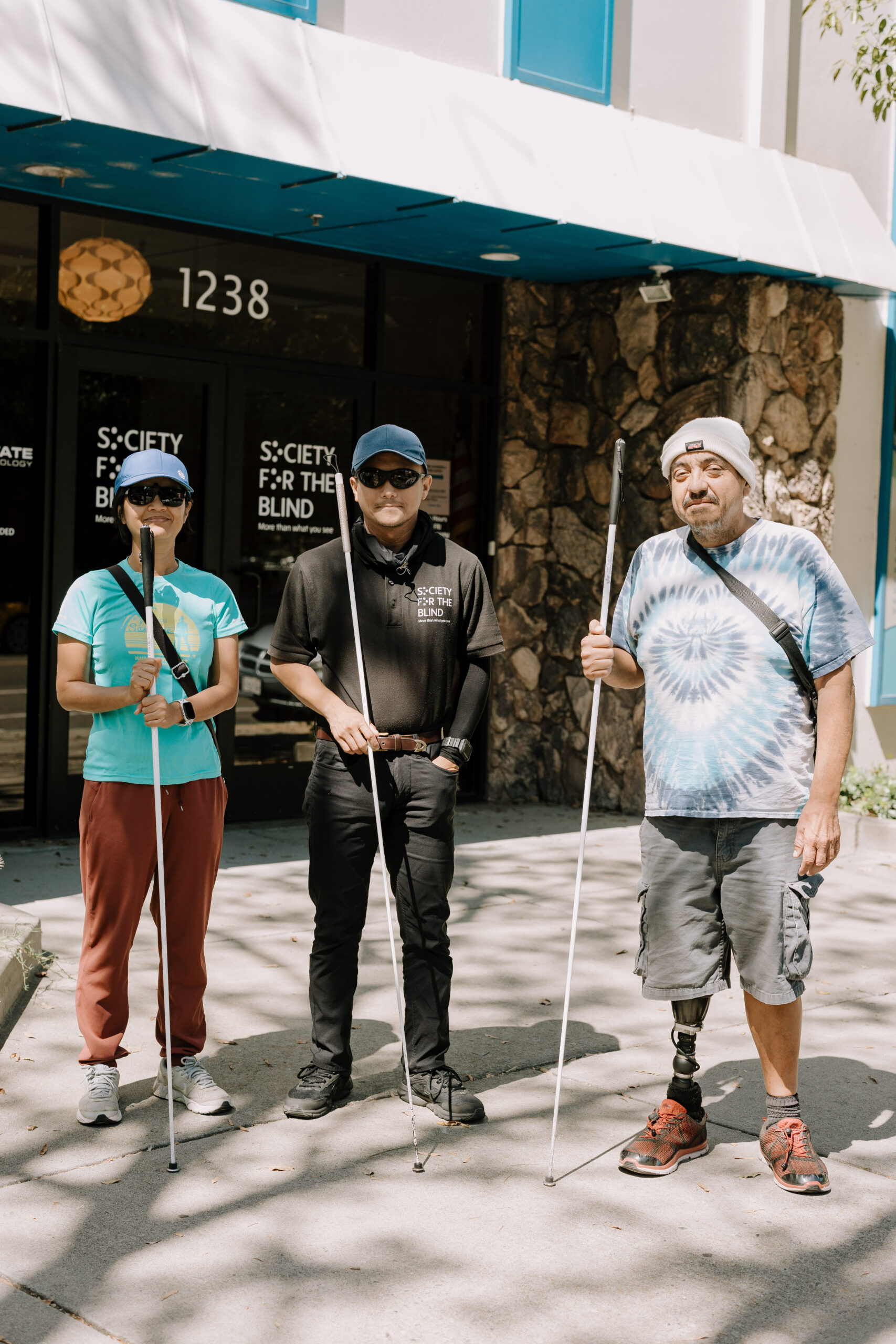 Three students at Society for the Blind pose with their white canes outside of the nonprofit entrance